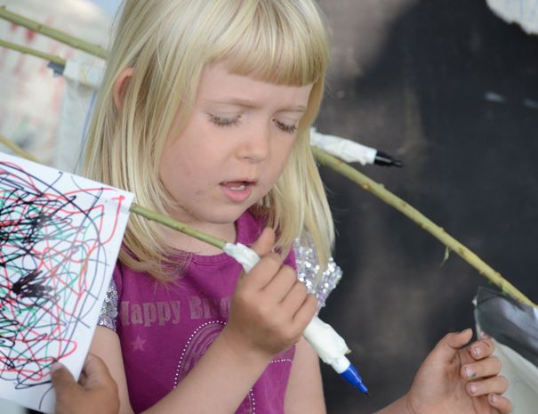 Et barn med blondt hår holder en pind indpakket i hvidt tape og et stykke papir med farverige kruseduller.