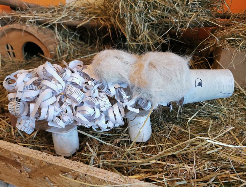 En skulptur af et får lavet af skrald, med en krop af plastikflasker og vinger af pap, står på en græsplæne.