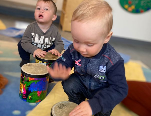 To børn leger med farverige trommer på et tæppe i et legerum.