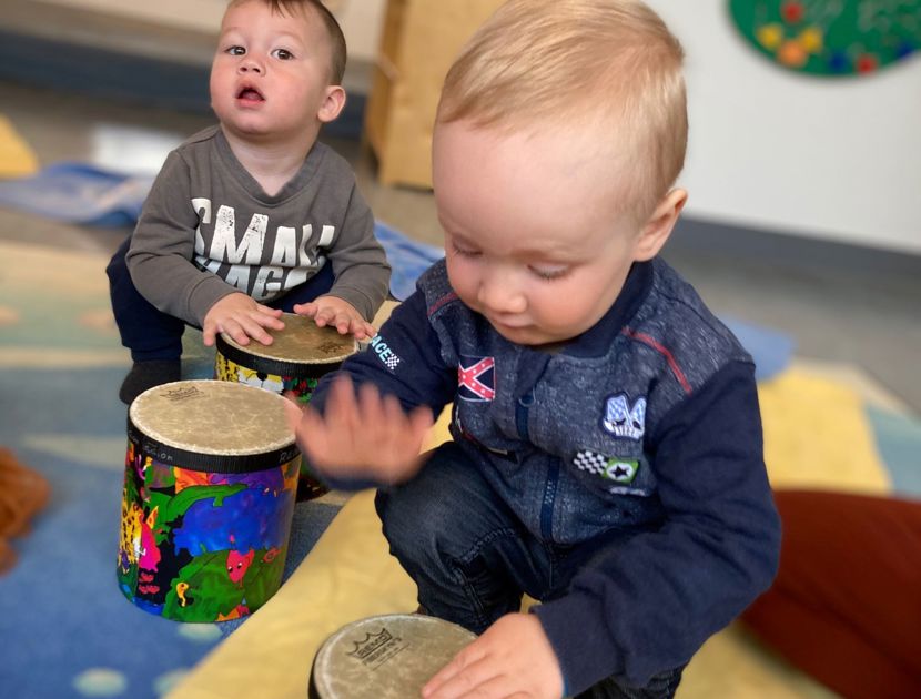 To børn leger med farverige trommer på et tæppe i et legerum.