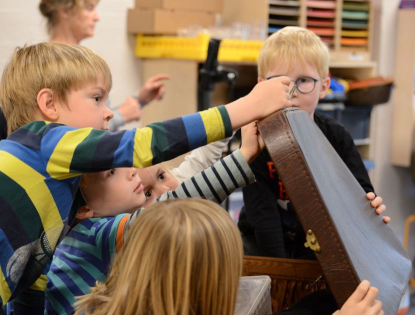 Børn samlet omkring en stor kuffert i et klasseværelse.