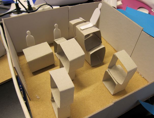 En model af et kontor med møbler lavet af pap, herunder skriveborde, stole og menneskelige figurer