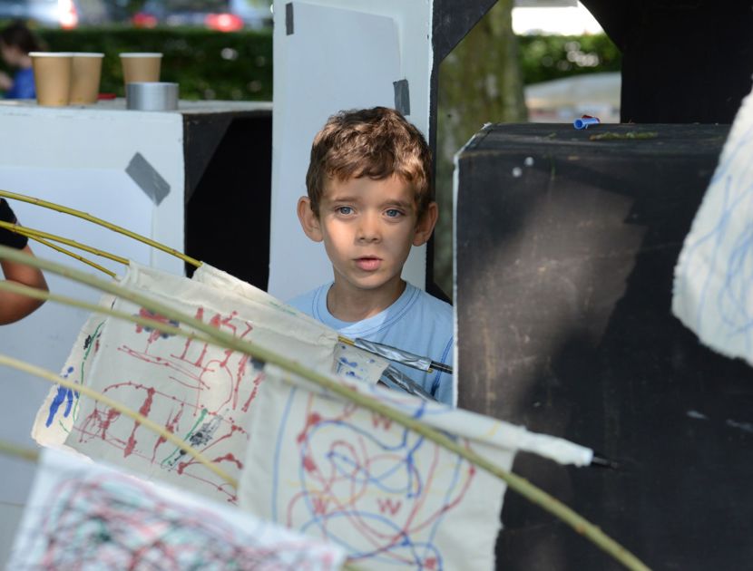Et barn står bag hængende kunstværker, som er abstrakte tegninger på papir. 