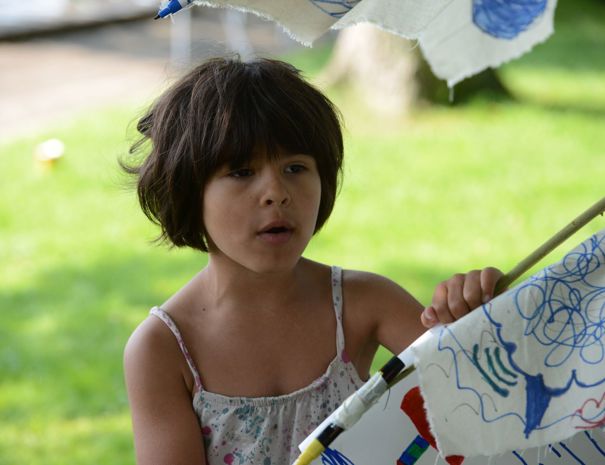 Udendørs holder et barn et stykke stof eller papir med forskellige tegninger og kruseduller.