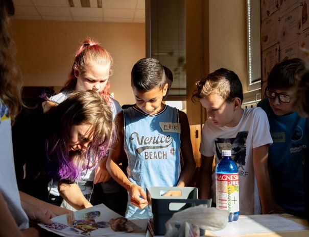 En gruppe børn er samlet omkring et bord med forskellige genstande, herunder papirer.